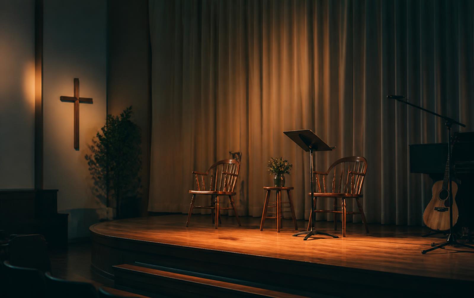 A quiet church stage lit with warm light, set with two chairs and a music stand